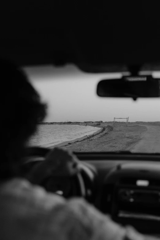 a black and white photo of a person driving a car, a black and white photo, by Nathalie Rattner, unsplash, conceptual art, in the desert beside the gulf, road to the sea, concert, farming