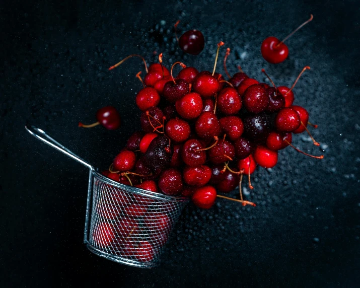 a metal strainer filled with cherries on a black surface, by Adam Marczyński, pexels, candy apple, red hoods, promo image