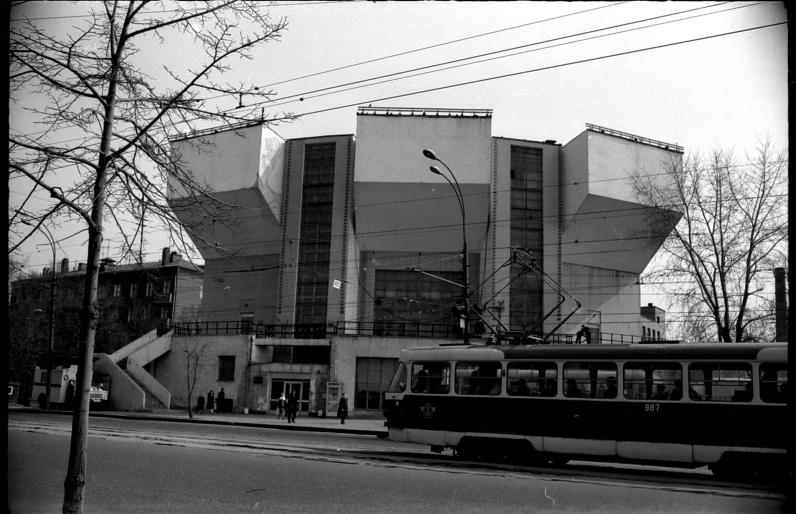 a black and white photo of a bus in front of a building, by Maurycy Gottlieb, brutalism, in moscow centre, concert hall, front and side views, tram