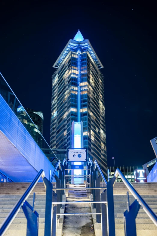 a set of stairs leading up to a tall building, inspired by Zaha Hadid, high blue lights, spaceport docking bay at night, towering over a city, ultrastation hq