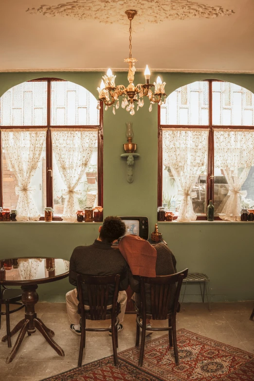 a couple of people that are sitting at a table, by Elsa Bleda, pexels contest winner, art nouveau, cozy environment, man sitting facing away, colonial style, green and brown color palette