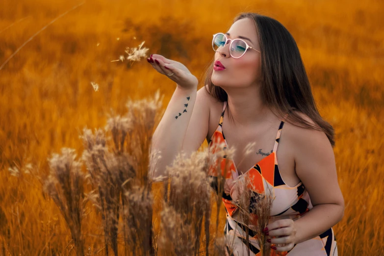 a woman blowing a flower in a field, a portrait, by Julia Pishtar, pexels contest winner, with square glasses, orange grass, avatar image, sexy girl