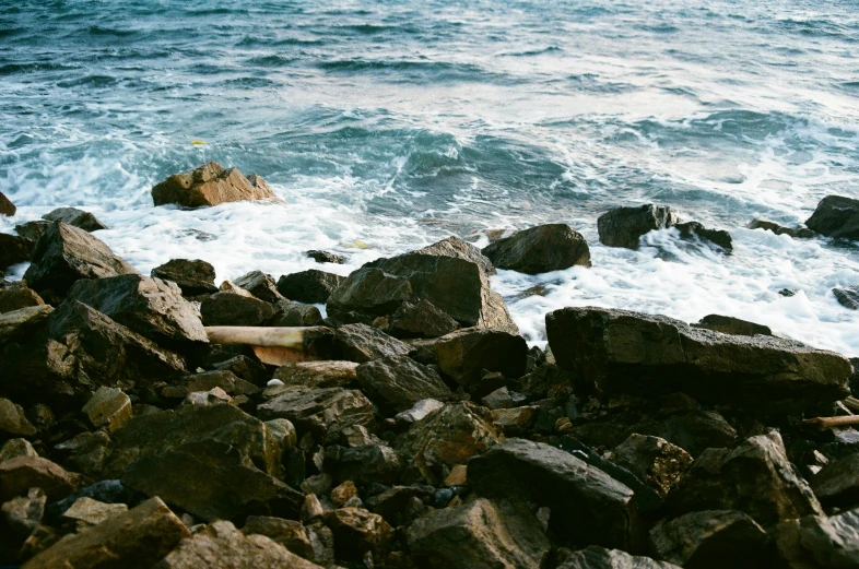 a man riding a surfboard on top of a rocky beach, an album cover, unsplash, romanticism, ((rocks)), brown, charybdis, spots