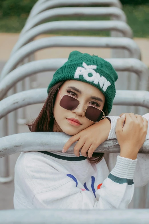 a woman leaning on a metal rail wearing a green hat and sunglasses, inspired by Ren Hang, trending on pexels, pop art, wearing a beanie, pony, icon, kenny wong x pop mart