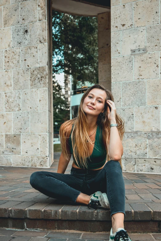 a woman sitting on steps talking on a cell phone, a picture, by Robbie Trevino, pexels contest winner, she is wearing a black tank top, satisfied pose, brunette with dyed blonde hair, kneeling and looking up