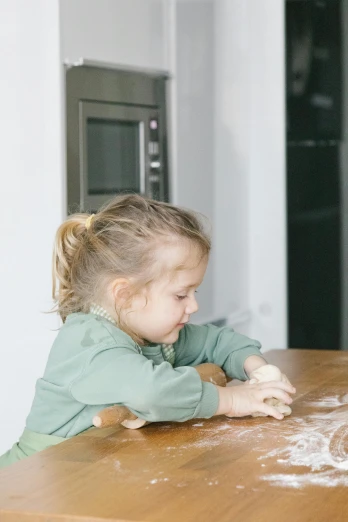 a little girl that is sitting at a table, covered in white flour, sitting on top a table