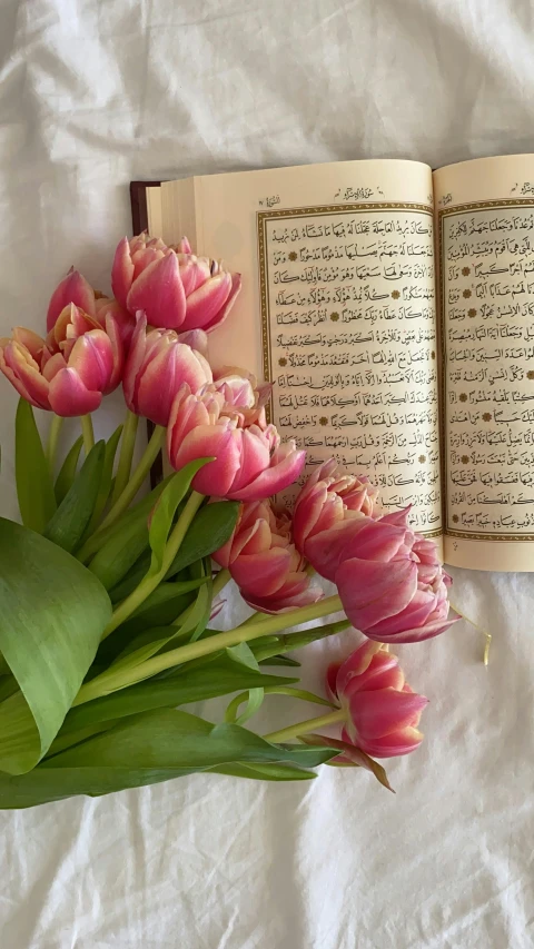 an open book sitting on top of a bed next to a bouquet of flowers, inspired by Maryam Hashemi, hurufiyya, tulip, romanized: al-kaʿbah, museum quality photo