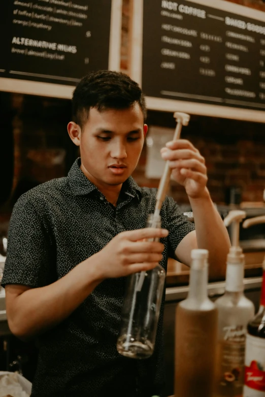 a man standing in front of a counter holding a bottle, pexels contest winner, aussie baristas, profile image, asian male, holding a wooden staff