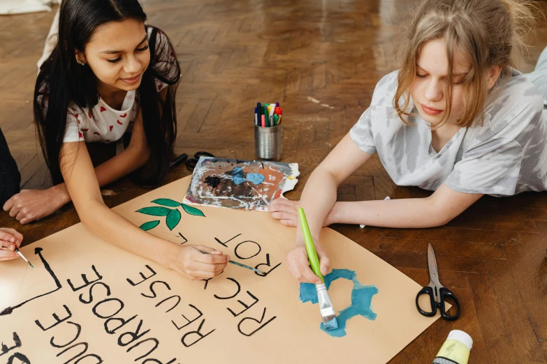 a group of young girls sitting on top of a wooden floor, a child's drawing, trending on pexels, action painting, subject action: holding sign, banner, a painting of two people, sustainable materials