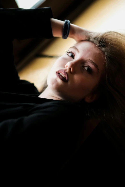 a woman laying on top of a wooden floor next to a window, a portrait, inspired by Elsa Bleda, unsplash, in a black hoodie, brown-blond-hair pretty face, pouty lips, grim fashion model looking up