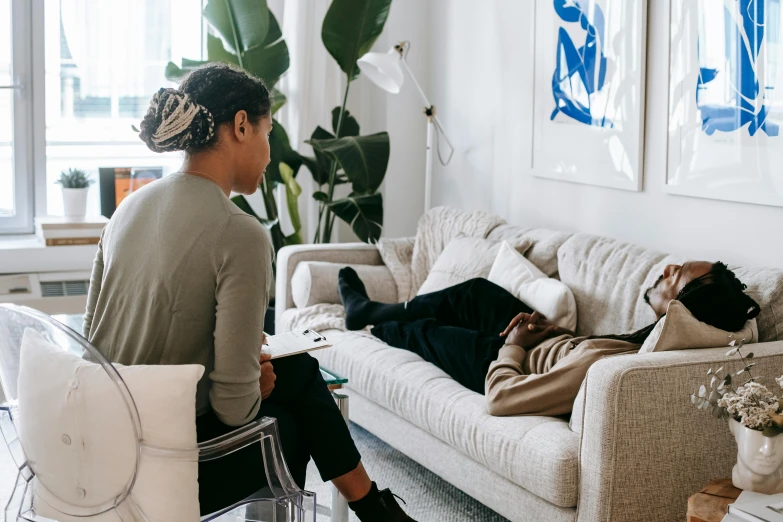 a woman sitting on top of a couch next to a man, by Carey Morris, pexels contest winner, acupuncture treatment, aida muluneh, on a white table, couch desk