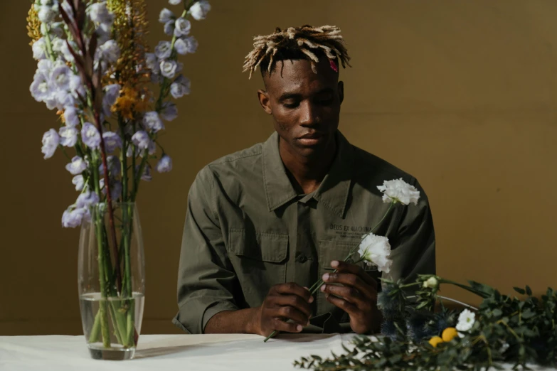 a man sitting at a table with flowers in front of him, inspired by Barthélemy Menn, pexels contest winner, ashteroth, medium long shot, xxxtentacion, ( ( theatrical ) )