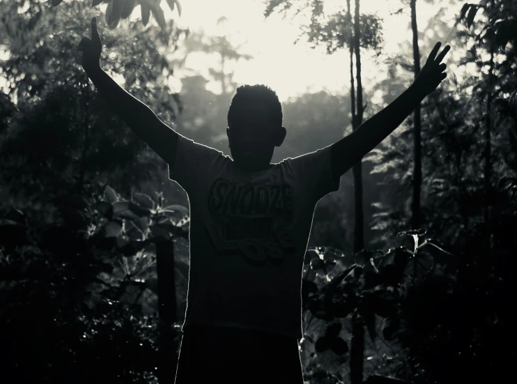 a black and white photo of a man with his hands in the air, pexels contest winner, sumatraism, in front of a forest background, character silhouette, backlighted, african man