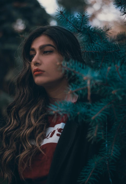 a woman standing in front of a pine tree, inspired by Elsa Bleda, trending on pexels, long wavy dark hair, hindu aesthetic, pouty lips, woman in streetwear