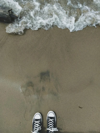 a person standing on a beach next to the ocean, wearing white sneakers, photograph from above, instagram story, wet floors