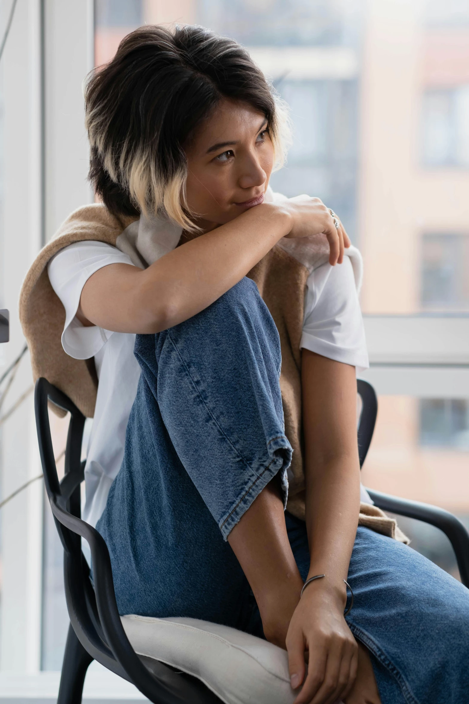 a woman sitting on top of a chair next to a window, trending on pexels, wearing denim, asian male, tired expression, androgynous person