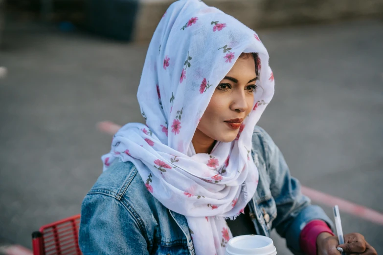 a woman sitting at a table with a cup of coffee, a portrait, trending on pexels, head scarf, wearing pink floral chiton, white scarf, girl wearing hoodie