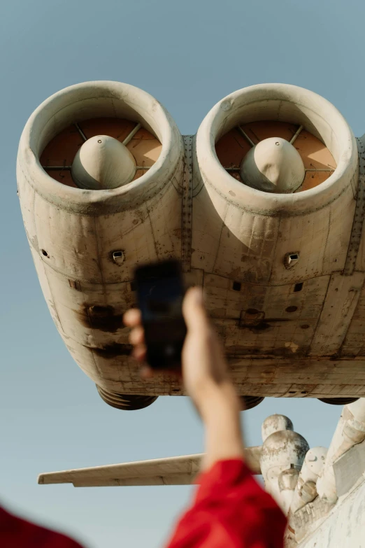 a person taking a picture of an airplane, a surrealist sculpture, inspired by Filip Hodas, unsplash, still from the mandalorian show, giant speakers, bottom view ， bladerunner, tatooine