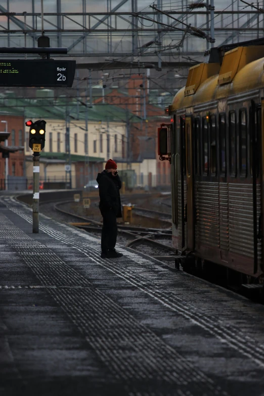 a train traveling down train tracks next to a train station, a picture, inspired by Tom Roberts, happening, north melbourne street, standing in the rain, person in foreground, cold lighting