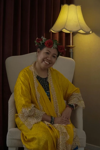 a woman sitting in a chair with a flower crown on her head, inspired by Ruth Jên, yellow robes, while smiling for a photograph, south east asian with round face, at the sitting couch