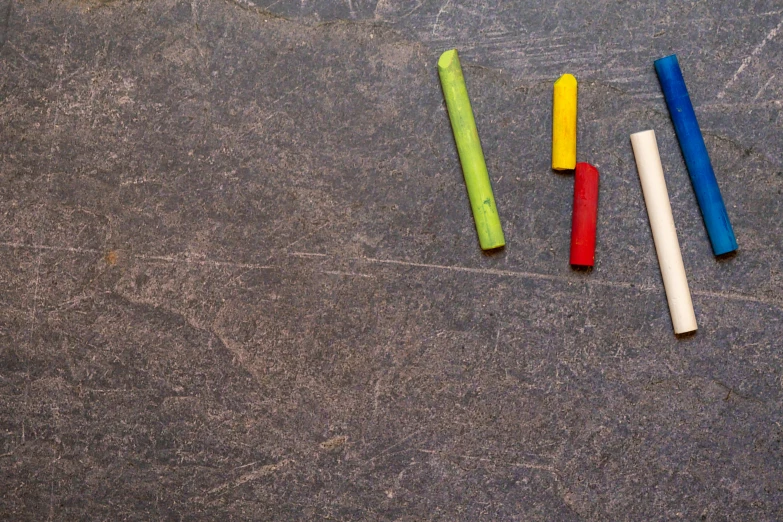 a group of colored chalk sticks sitting next to each other, a child's drawing, inspired by Jan Rustem, graffiti, background image, slate, shot with sony alpha, studio floor