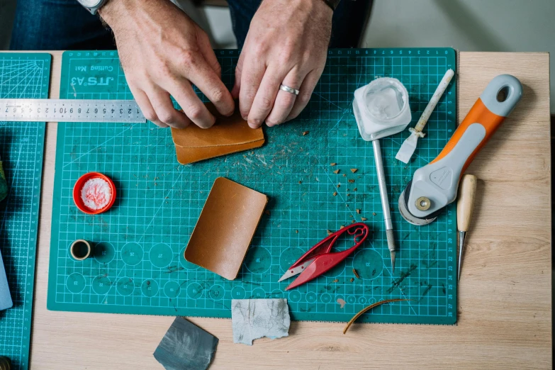 a man is working on a piece of leather, a still life, trending on unsplash, arts and crafts movement, 9 9 designs, teal aesthetic, scrap metal on workbenches, business card