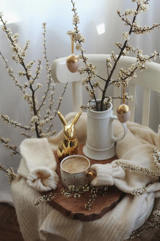 a wooden table topped with a vase filled with flowers, inspired by Lili Árkayné Sztehló, trending on reddit, with a cup of hot chocolate, bunny, gold and silver and brass, studio photo