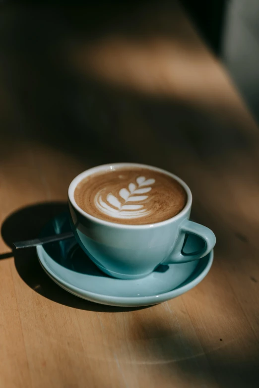 a cup of coffee sitting on top of a wooden table, by Austin English, light blue, thumbnail, latte art, multiple stories