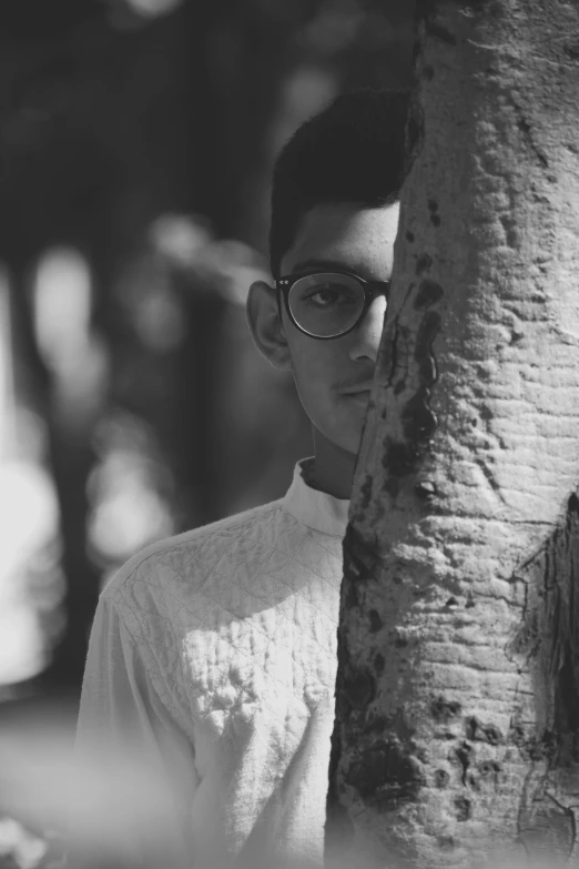 a black and white photo of a man leaning against a tree, inspired by Sergio Larraín, jewish young man with glasses, indian, in a temple, ((portrait))