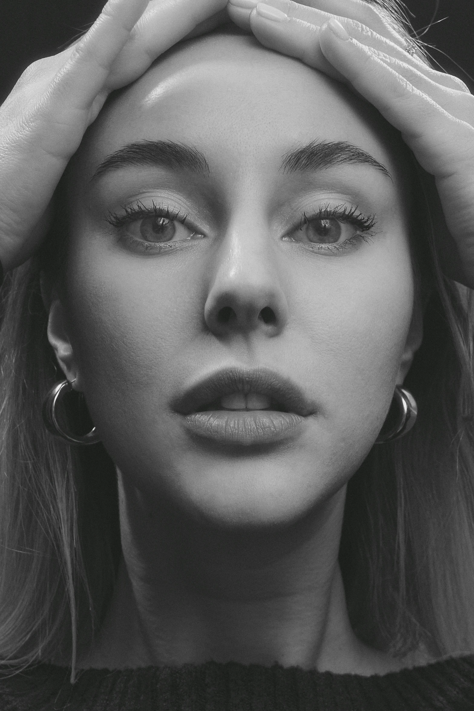 a black and white photo of a woman with her hands on her head, inspired by Maud Naftel, trending on pexels, hyperrealism, sydney sweeney, alternate album cover, close - up of face, music video