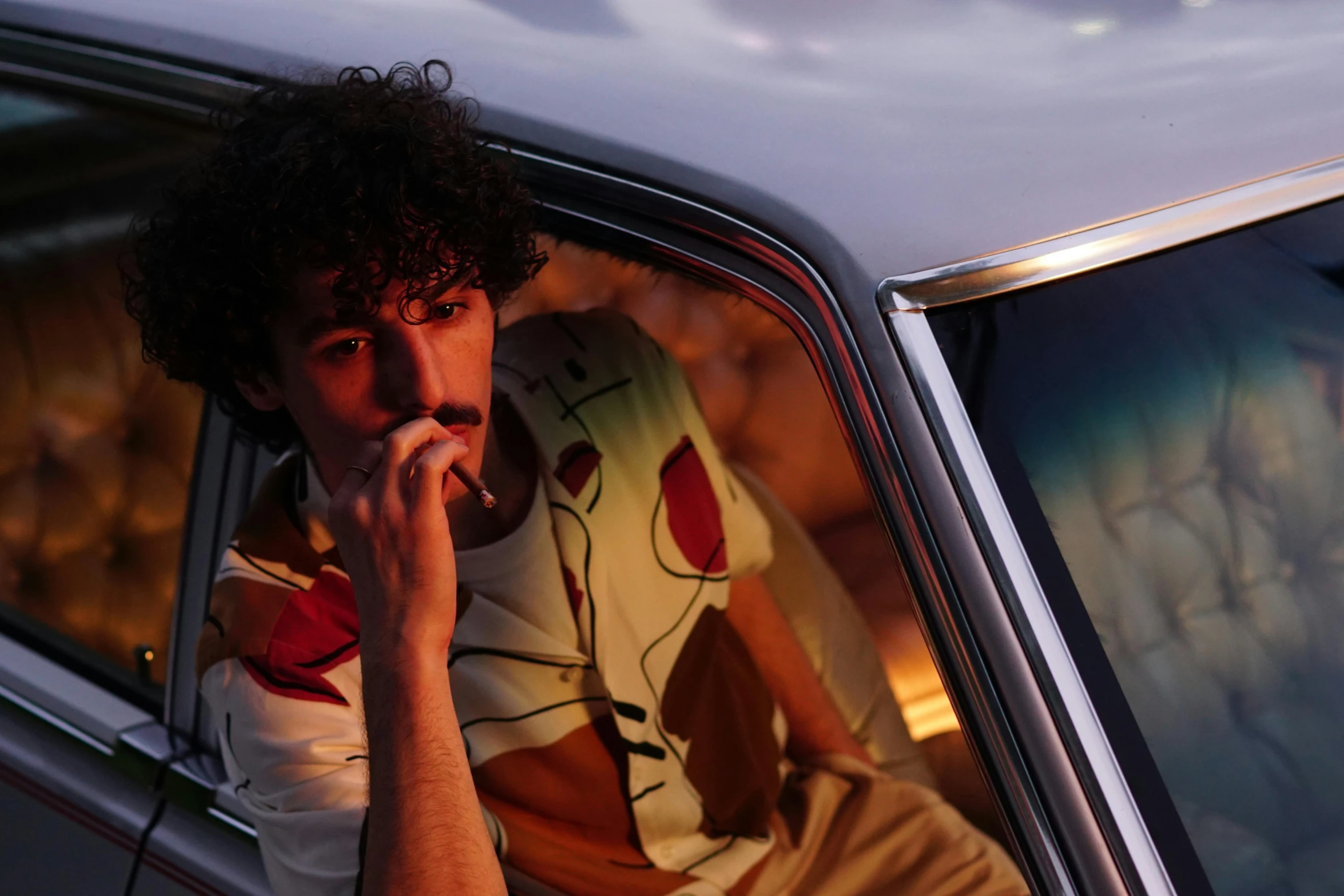 a man sitting in the passenger seat of a car, inspired by Nan Goldin, pexels contest winner, patterned clothing, curls on top, daniel ricciardo, promotional image