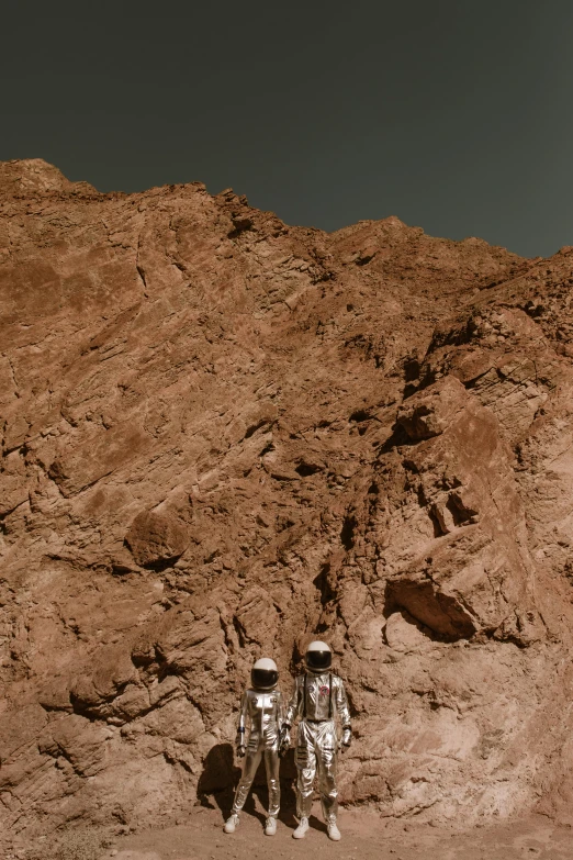 a couple of people that are standing in the dirt, a colorized photo, by Philip de Koninck, unsplash, martian landscape, red sea, silver space suit, cliffs