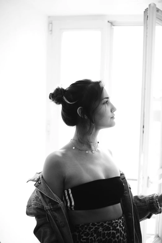 a black and white photo of a woman looking out a window, a black and white photo, unsplash, dua lipa, demi moore, her hair pinned up, backlight body