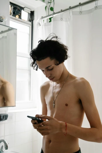 a man standing in front of a bathroom mirror looking at his cell phone, inspired by Nan Goldin, trending on pexels, wearing bra, boy has short black hair, teenage boy, non binary model