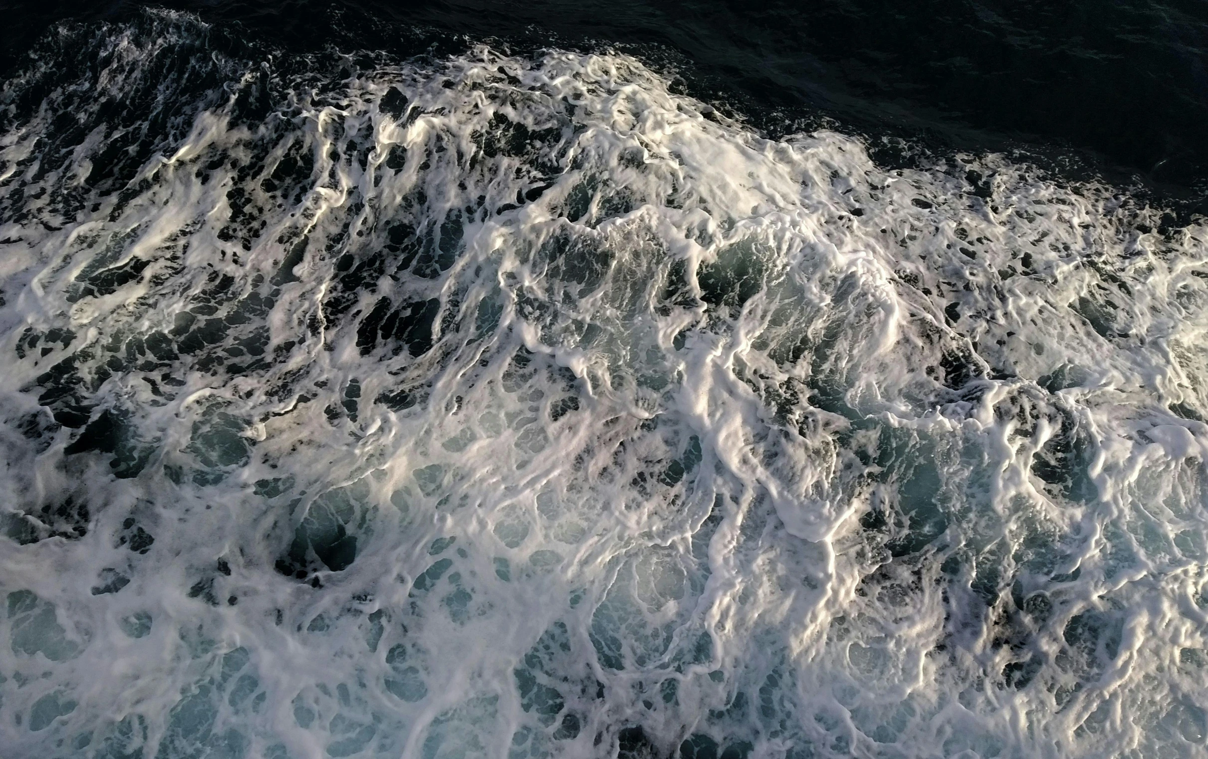 a man riding a surfboard on top of a wave, by Robert Sivell, pexels, photorealism, sea foam, lit from above, photo taken from a boat, oil on water