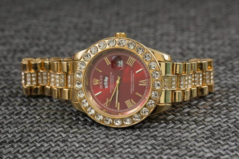 a close up of a watch on a table, pexels contest winner, renaissance, red and gold, chief keef, with sparkling gems on top, 3/4 view realistic