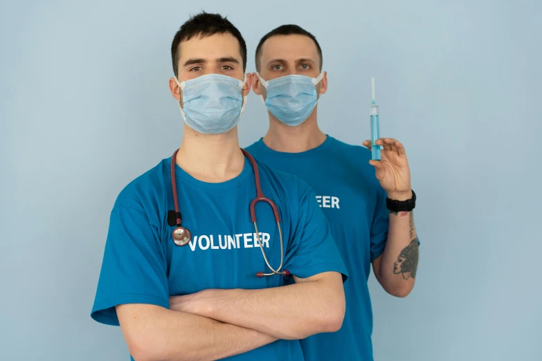 a couple of men standing next to each other, holding a syringe, background image, scrubs, 2 people