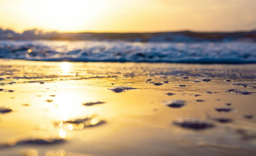 the sun is setting over the water on the beach, unsplash, gold refractions off water, laying on sand, australian beach, resin