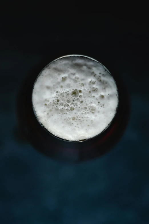 a glass of beer sitting on top of a table, a microscopic photo, by Andrew Domachowski, pexels, process art, white foam, dark and dim, round-cropped, blue