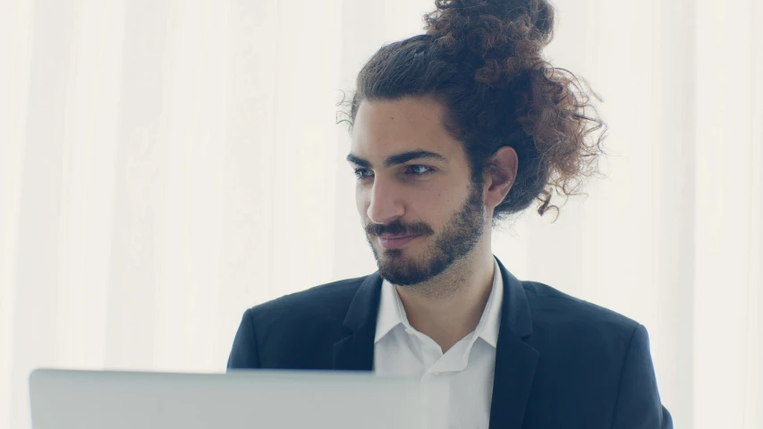 a man sitting in front of a laptop computer, inspired by Cricorps Grégoire, pexels contest winner, long curly hair intricate, topknot, professional profile picture, androgynous male