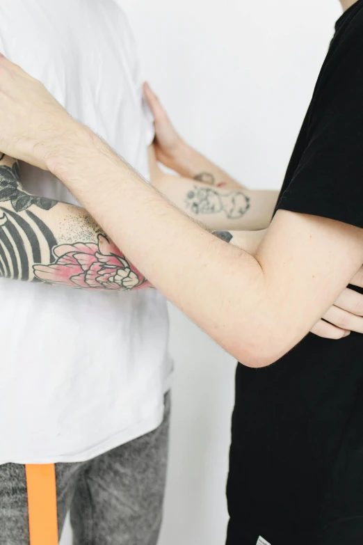 a man standing next to a woman with a tattoo on her arm, by Jessie Alexandra Dick, trending on unsplash, aestheticism, two men hugging, on a pale background, teenage boy, facing each other