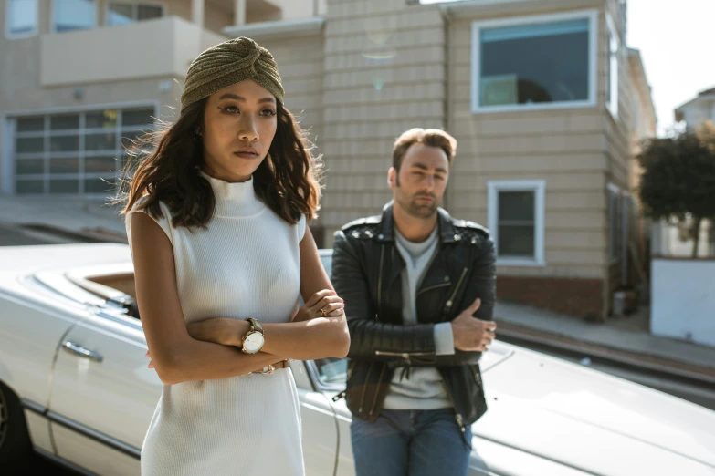 a man and a woman standing in front of a car, janice sung, an olive skinned, white, looking serious