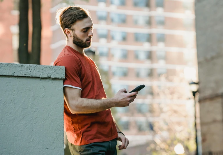 a man standing on a ledge looking at his cell phone, trending on pexels, red shirt brown pants, ponytail and beard, avatar image, max dennison