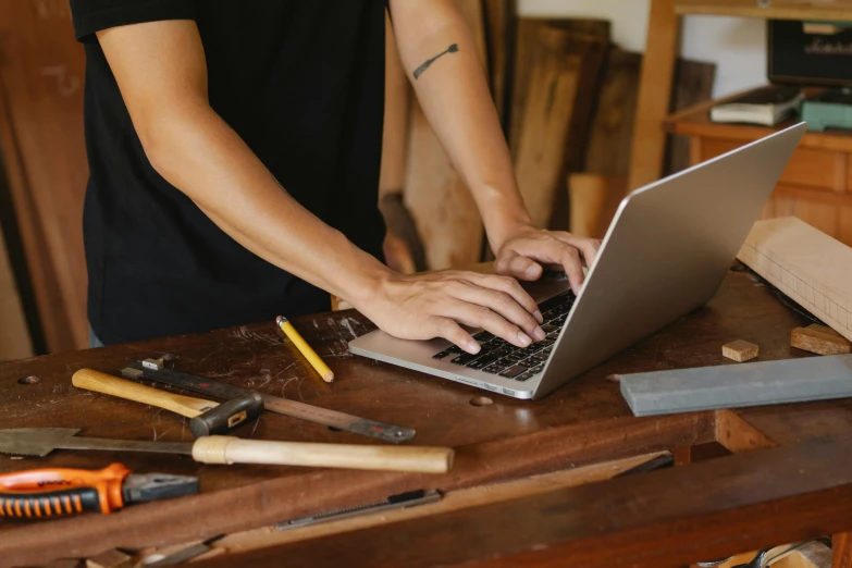 a woman using a laptop computer on a workbench, by Carey Morris, trending on pexels, arts and crafts movement, a handsome, with a wooden stuff, wood and gold details, where a large