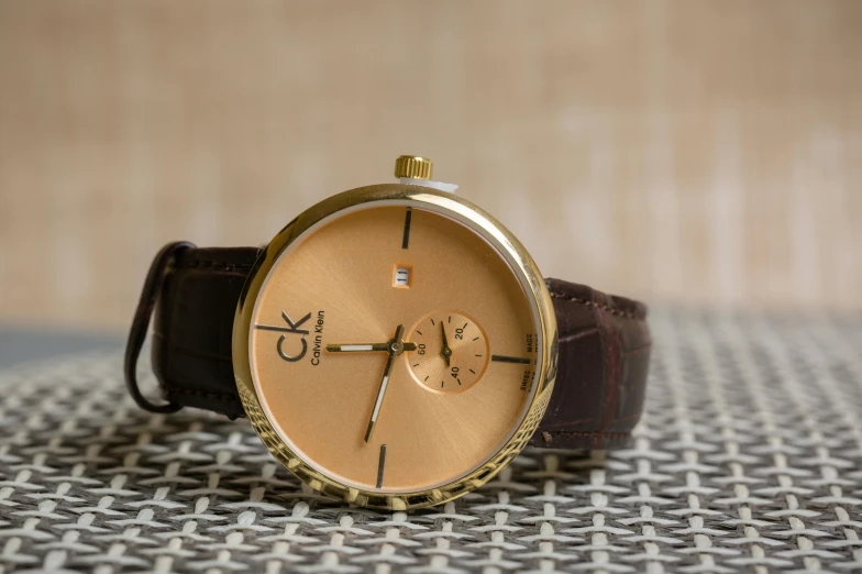 a close up of a watch on a table, an album cover, inspired by Charles Le Roux, trending on unsplash, arabesque, calvin klein photography, brown and gold color palette, calvin klein, grain”