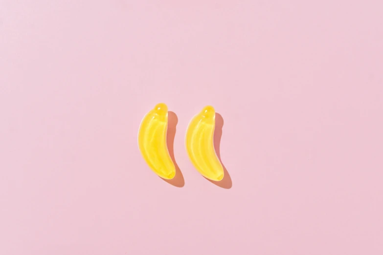 two bananas sitting next to each other on a pink surface, by Julia Pishtar, trending on pexels, polymer clay earrings, transparent background, from the waist up, mono-yellow
