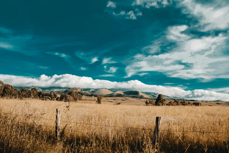 a field with a fence and mountains in the background, by Peter Churcher, unsplash, visual art, kahikatea, background image, slightly tanned, blue skies