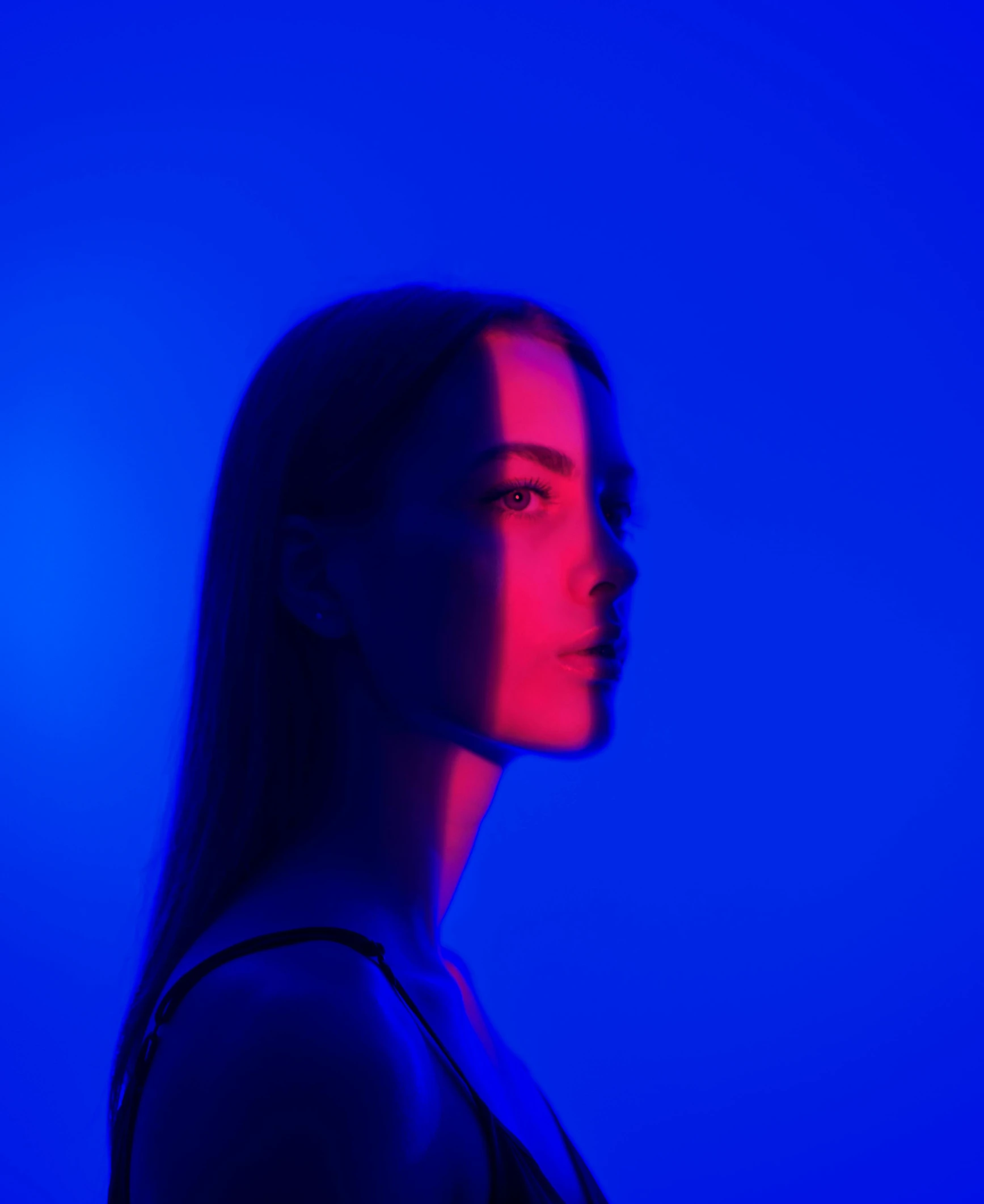 a woman standing in front of a blue background, an album cover, inspired by Elsa Bleda, color field, blue and red lights, looking away from camera, bella poarch, asher duran
