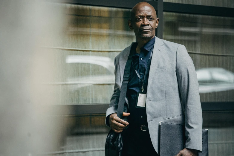 a man in a suit standing in front of a building, by Bernard Meninsky, pexels contest winner, samuel jackson, lena oxton, detective clothes, leaning on door