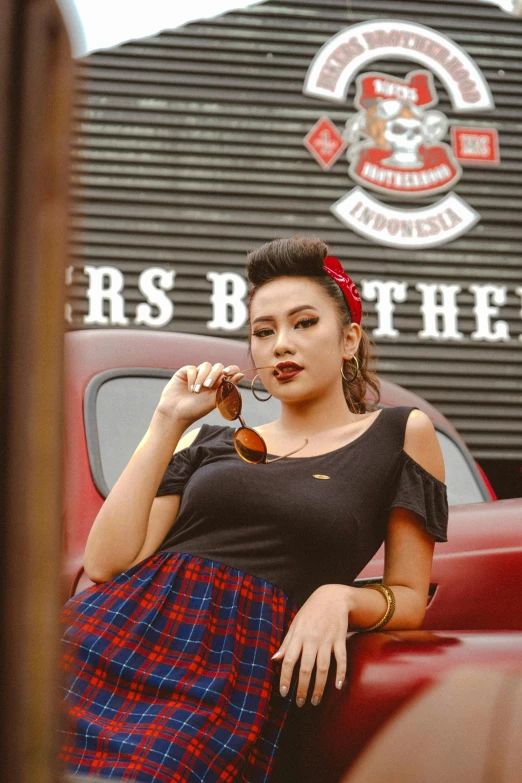 a woman sitting on the back of a red truck, a portrait, inspired by Rudy Siswanto, instagram, sumatraism, rockabilly style, fashion shoot 8k, plaid skirt, official screenshot